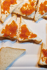 Sandwiches with red caviar and creamy cheese on the white plate. Vertical photo closeup. Russian cuisine.