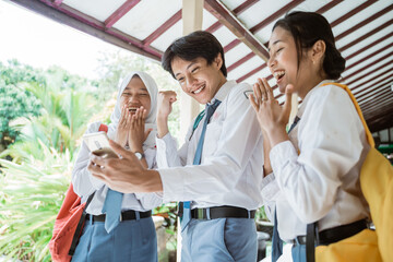 Obraz premium three Indonesian high school students look at the screen using one smartphone to see the announcement of graduation together at school