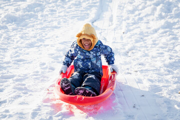 Cute boy child happily riding downhill on a toboggan sled