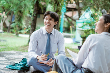 a boy in high school uniform smiling when discuss together sitting on the floor at school garden