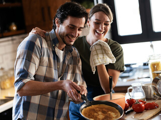 Boyfriend and girlfriend making pancakes at home. Young couple having fun in the kitchen