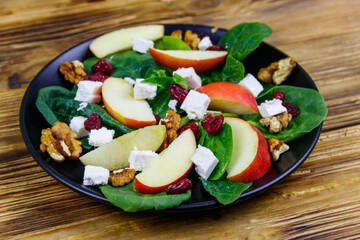 Autumn spinach salad with apple, feta cheese, walnut and dried cranberry on wooden table. Healthy vegetarian food