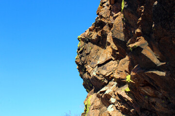 Weathered Lichen Covered Sheer Rock on Top of Cliff against Blue Sky 