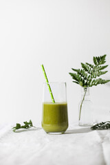 Green smoothie in a glass with a straw on a light background. The concept of healthy eating. Copy space.