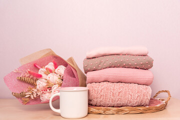 Stack of folded wool knitted sweaters or pullovers in pink pastel colors and mag on table with...