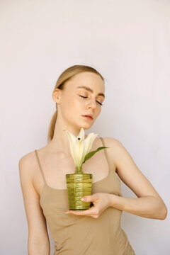 Sensual portrait of a young blond girl with a litle vase and a lily in it