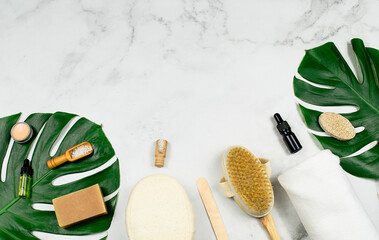 Natural spa cosmetics products, massage brush, sea salt and tropic monstera leaves on white background.