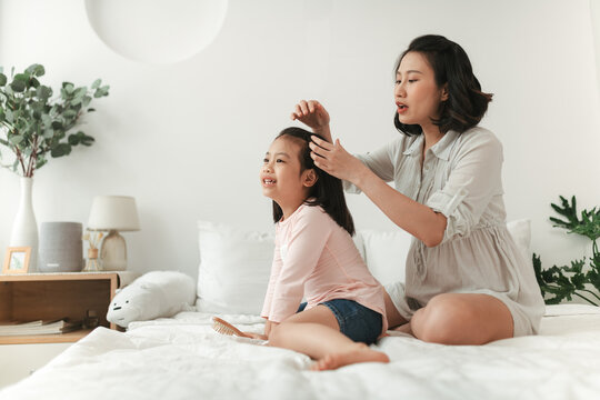 Adorable young family in living room. Mother combing her daughter's hair. Happiness and love concept