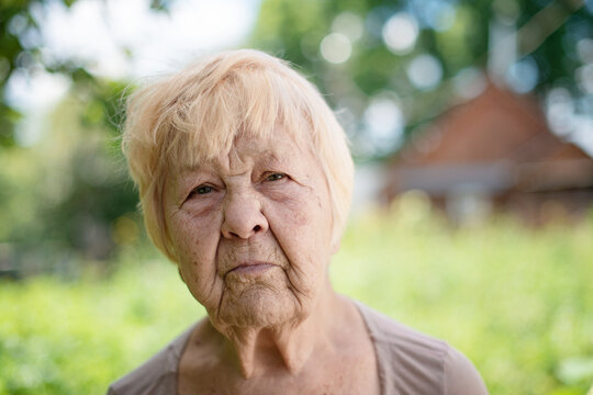 Portrait of an old wrinkled woman of a 90-year-old grandmother with a serious expression on her face in nature in the summer.