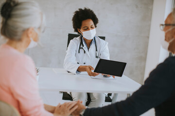 Senior couple with protective facial masks receive news from black female doctor