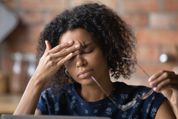 Frustrated black female freelancer overworked by computer feel headache migraine take off eyewear rub nose bridge. Exhausted tired young biracial lady suffer of eye pain vision problem chronic fatigue - Powered by Adobe