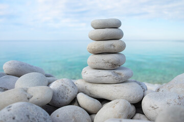 Fototapeta na wymiar Flat rocks stacked on top of each other standing vertically on the beach, blue water and sky out of focus in the background, soft light. Balance, harmony, relaxation and peace concept. Space for copy.