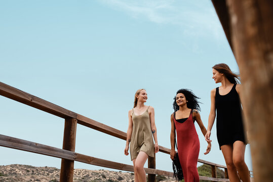 Young diverse girlfriends walking on wooden path against sky