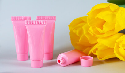 Plastic pink cosmetic tubes next to yellow tulip flowers