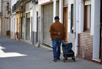 Obraz na płótnie Canvas An elder man walks with his shopping trolley in an alley in Jalo´n-Spain.