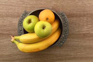 Antique bowl with bananas, apples and lemons on wooden table. Top view.