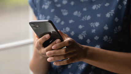 Close up view of modern mobile phone device in hands of young african american female user. Modern day teen black lady hold digital gadget chat via wifi internet use application browse social networks