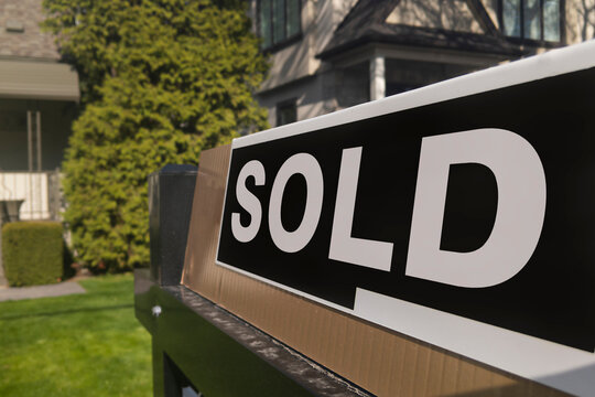 Sign sold in front of a detached house in residential area. Real estate bubble, hot housing market, overpriced property, buyer activity, spring and summer sale  concept.