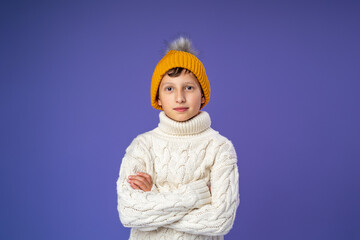 happy, cheerful, smiling child in a knitted sweater and a yellow knitted hat on a purple background. the child has put on bright warm clothes and is happy about the beginning of winter. Copy space.