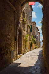 Beautiful alley with medieval houses framed by arch, Pienza, Italy