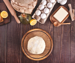 Ingredients for home baking, kitchen utensil and baking raw dough on the wooden background. Top view. Copy space.