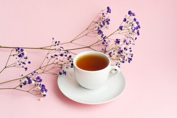 Small white gypsophila flowers on a pink pastel background with a cup of tea, space for text