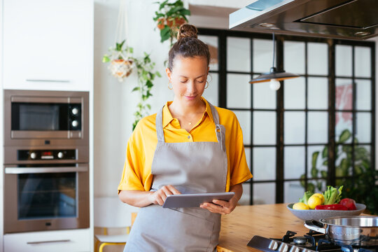 Relaxed woman in apron surfing tablet in kitchen