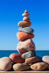 Rock zen pyramid of white and pink pebbles on a background of blue sky and sea.