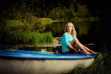 Fototapeta na wymiar blonde girl sitting on a blue boat by the water, selective focus