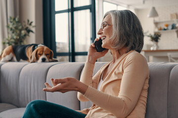 Side view of good looking senior woman in casual clothing talking on the smart phone and smiling...