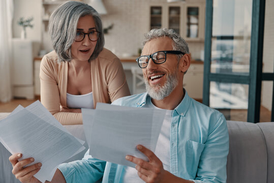 Modern senior couple in casual clothing taking care of their taxes while bonding together at home