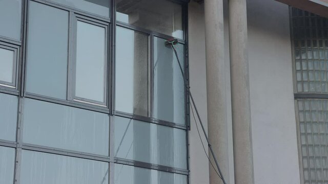 Cleaning a high window wit a long broom using osmoses water for professional  windows cleaning