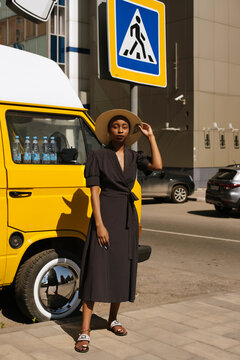 City portrait of a black girl in a polka dot dress and a hat near the yellow van