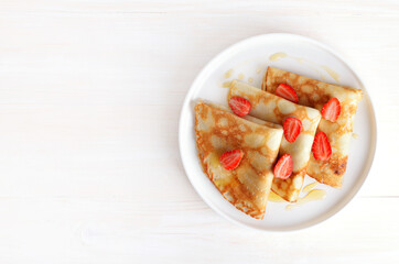 Crepes with strawberry and honey on white plate