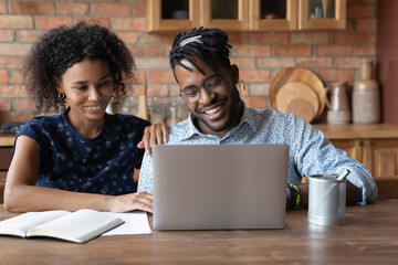 Happy african american family couple sit at home office by pc choose house renovation design watch...
