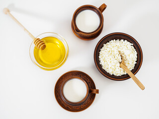 Breakfast in handmade earthenware on a white background. Natural farm dairy products, fresh cottage cheese and cow's milk. Flower honey in a glass bowl. Pottery. Top view, flat lay