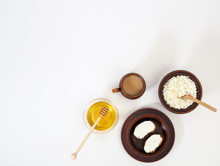 A beautiful composition of a healthy breakfast with farm dairy products and natural honey in earthenware dishes. A cup of coffee, honey, sandwiches with curd cheese and cottage cheese on a white