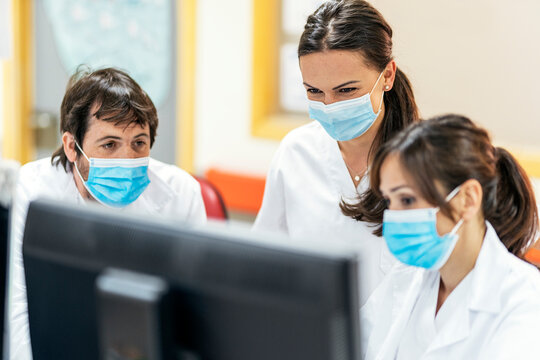 Group of Doctors In Uniforms And Masks Using Computer At Table