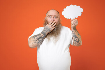 Fat shock pudge obese chubby overweight tattoo bearded big belly man in white t-shirt hold empty blank Say cloud speech bubble promotional content cover mouth with hands isolated on orange background.
