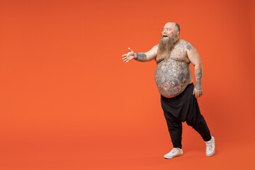 Full length side view of fat pudge obese chubby overweight tattooed bearded big belly man in pants naked torso stand with outstretched hand for greeting isolated on orange background studio portrait.