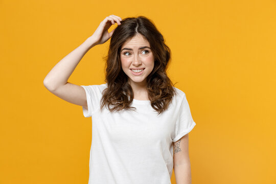 Young pensive thoughtful overthink mistaken troubled eueropean caucasian student woman 20s in white basic casual tshirt look aside sctratch head put hand isolated on yellow background studio portrait