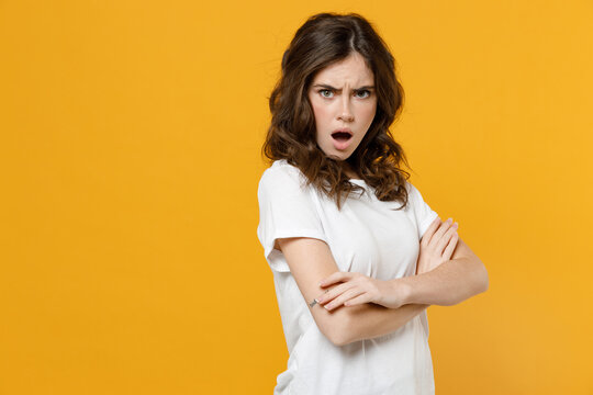 Young offended angry indignant frowning caucasian student woman 20s in white basic t-shirt look camera with open mouth hold hands crossed folded isolated on yellow orange background studio portrait.