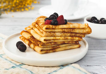 thin homemade pancakes with berries on plate.
