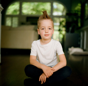 Handsome young boy with a mohawk haircut sitting on the floor