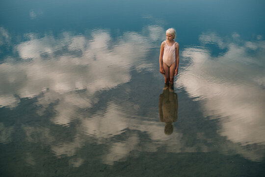 Little girl standing in the water where white clouds are reflected