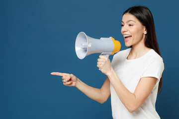 Young cute beautiful latin woman 20s wearing casual basic white t-shirt screaming hot news announces shout in megaphone point index finger aside isolated on dark blue color background studio portrait.