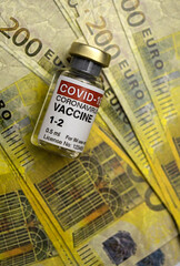 Covid-19 vaccine next to several two hundred euro banknotes, concept image
