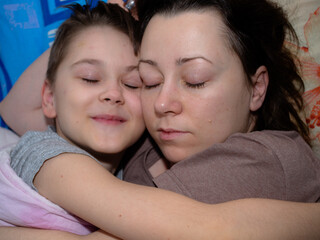 a young mother and son of 10 years old are sleeping in an embrace on the bed. a happy child.
