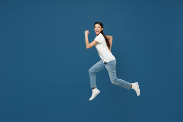 Fototapeta na wymiar Full length side view of young happy sport smiling brunette latin woman 20s wear white casual basic t-shirt running fast hurrying jumping high isolated on dark blue color background studio portrait