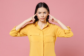 Young brunette nervous irritated stressed latin student woman 20s wearing yellow casual shirt covering ears with fingers hands looking camera isolated on pastel pink color background studio portrait.